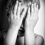 bambino che  si copre la faccia con le mani